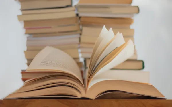 An open book, its pages fanning up, sits in front of two more stack of books