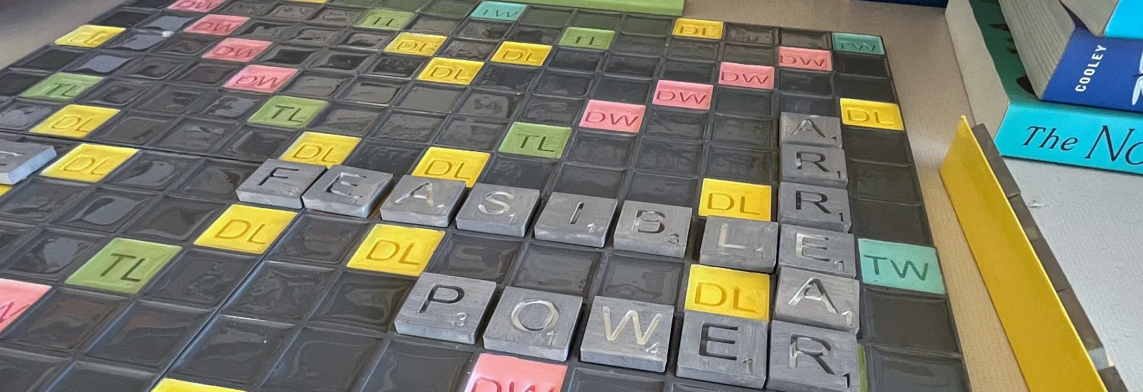 A colorful, 3D-printed Scrabble set in front of a stack of books